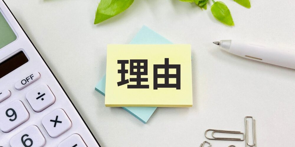電卓とペン、付箋やクリップが並ぶデスク上に黄色い付箋で「理由」と大きく書かれた付箋を置いた、説明理由を示すイメージ写真。