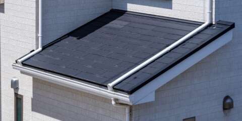 白い外壁に取り付けられた黒いタイル葺きの屋根部分をクローズアップ。雨樋や縁の金具が見え、強い日差しを浴びたシャープな屋根のディテールを写したイメージ