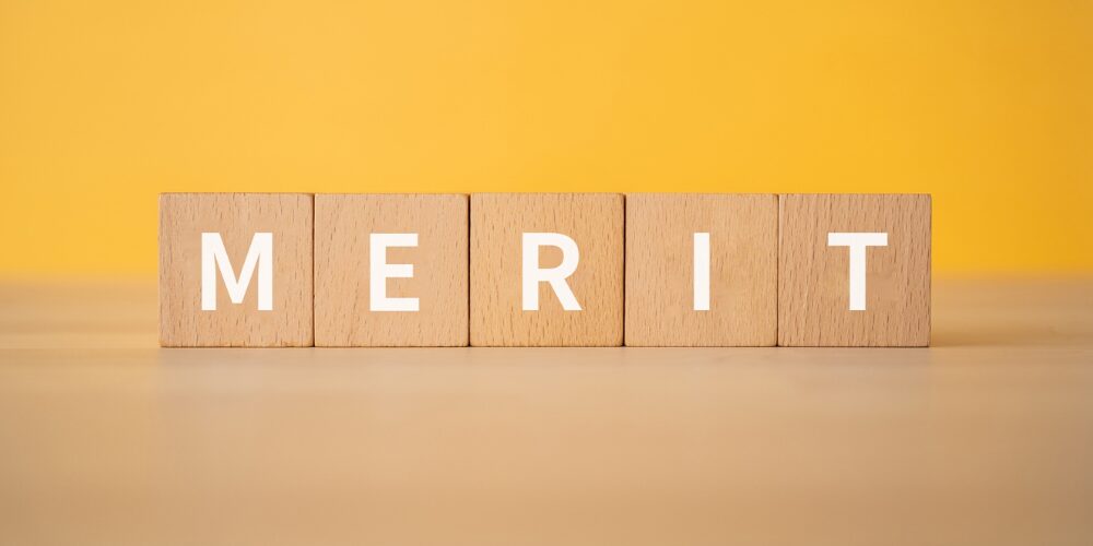 黄色背景に木製ブロックで構成された「MERIT」の文字。メリット・利点を強調するビジュアル
