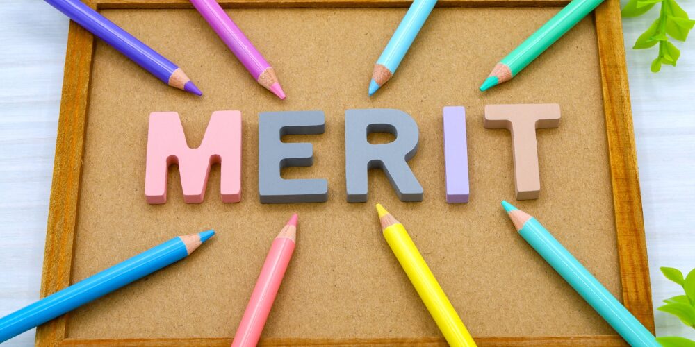 コルクボードの上にパステル調の立体文字で『MERIT』と並べられ、その周囲を色とりどりの色鉛筆が放射状に囲んでいるイメージ