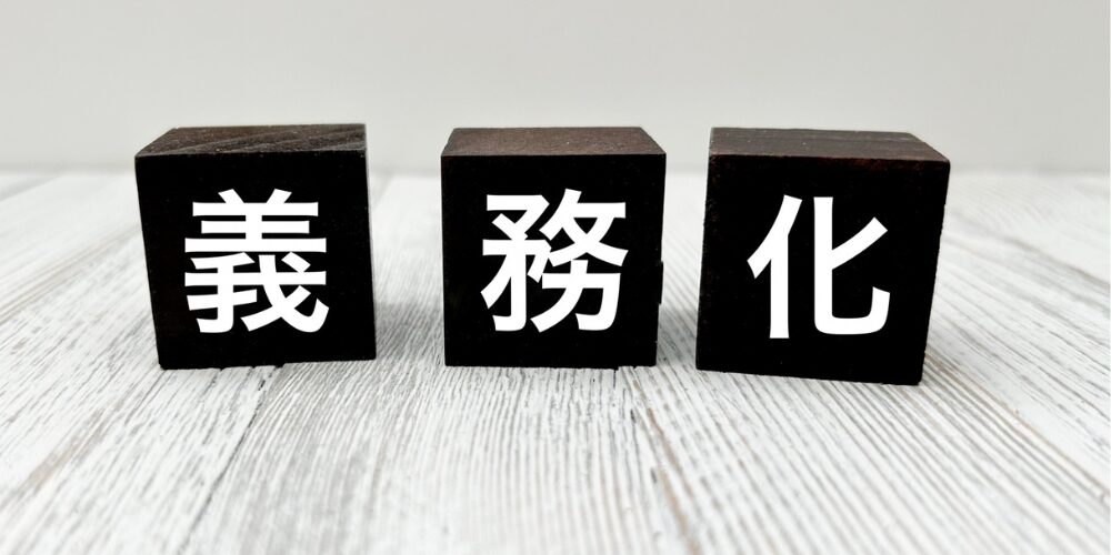 木製の黒いブロックが横並びに3つ置かれ、それぞれに白抜きの文字で「義」「務」「化」と書かれている写真