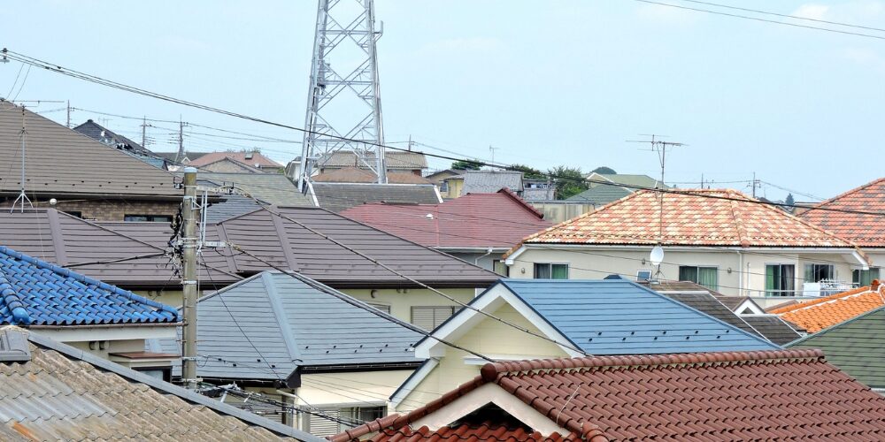住宅地を俯瞰で捉えた写真。色とりどりの瓦や金属屋根が連なり、電柱や送電線が錯綜する街並みの屋根群のイメージ